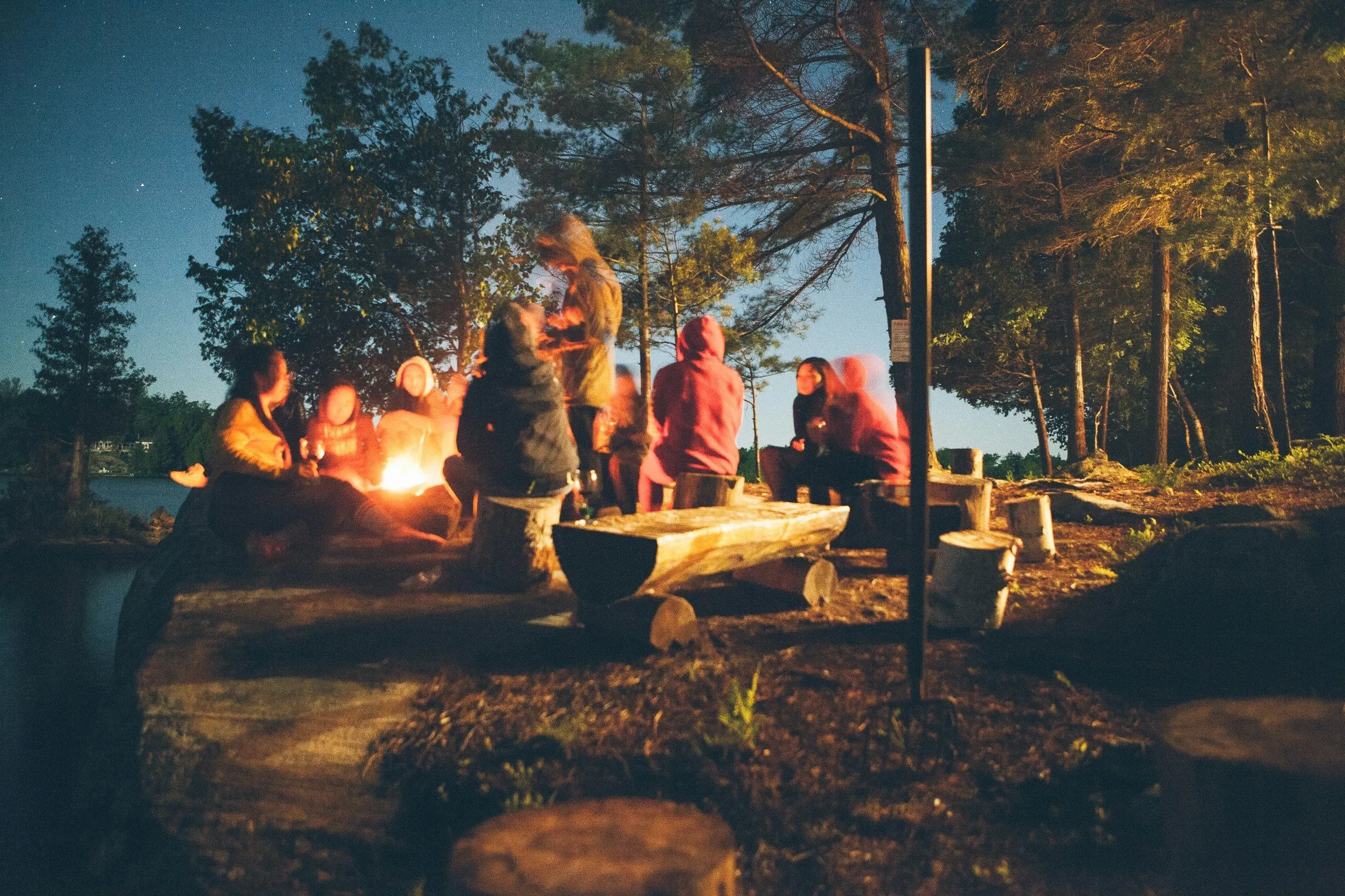 Campers gathered around a campfire at a lakeside campground in the evening